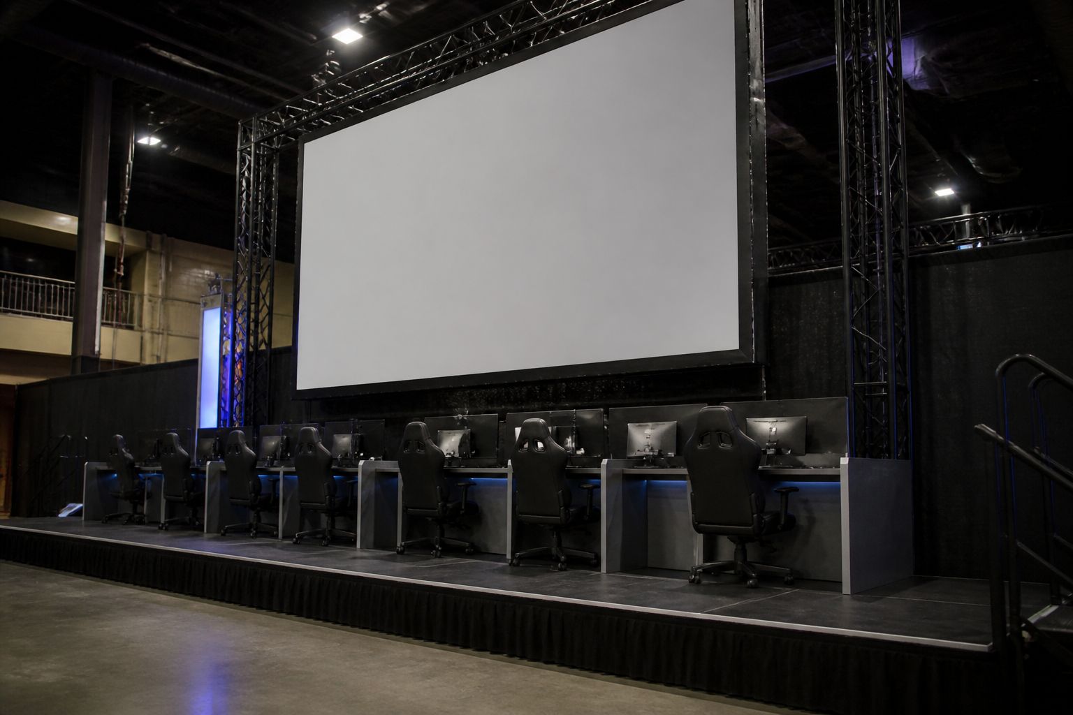Side angle of a small LAN tournament stage with a large blank screen and empty player seats